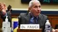 dr. fauci speaks from a table with his name sign and some water in front of him.
